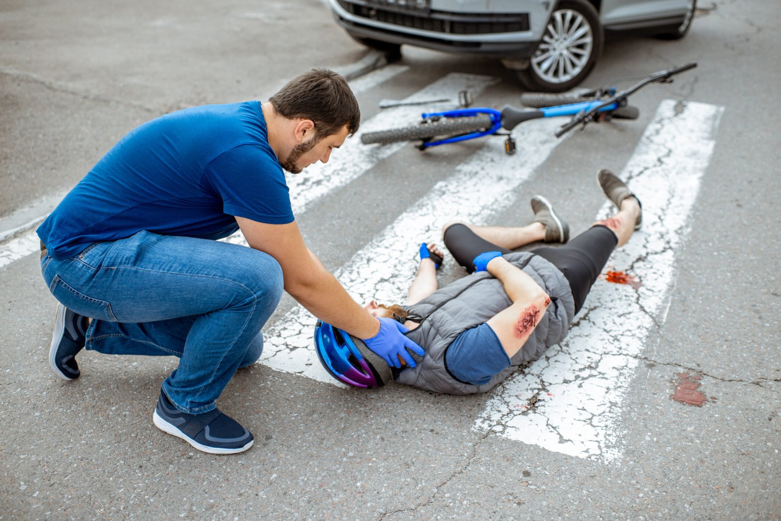 Road accident with injured cyclist on the pedestrian crossing with passerby pedestrian providing first aid fixing men's head